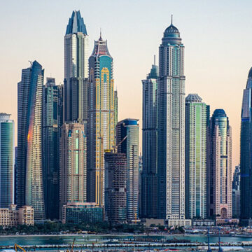Skyline of Dubai with a cluster of glass skyscrapers along the waterfront at sunset.